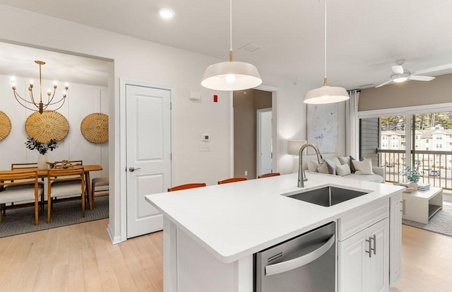 kitchen featuring stainless steel dishwasher, decorative light fixtures, a center island with sink, and sink