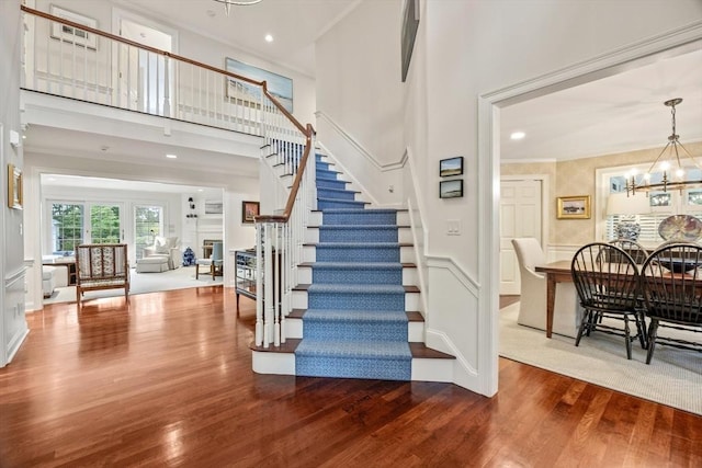 stairs featuring a chandelier, hardwood / wood-style floors, a towering ceiling, and ornamental molding