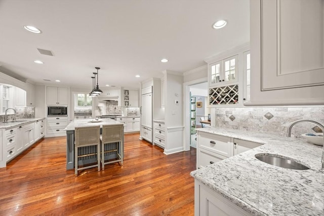 kitchen with built in appliances, white cabinetry, a center island, and sink