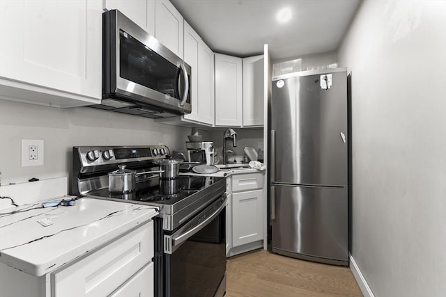 kitchen with light stone countertops, appliances with stainless steel finishes, white cabinetry, light wood-type flooring, and sink