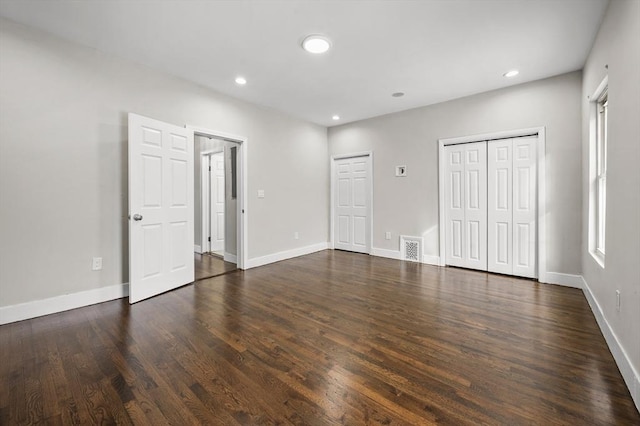 unfurnished bedroom featuring dark hardwood / wood-style floors and two closets