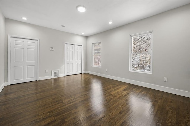 unfurnished bedroom with dark hardwood / wood-style floors and two closets