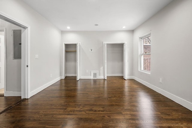 unfurnished bedroom featuring dark wood-type flooring, two closets, and electric panel