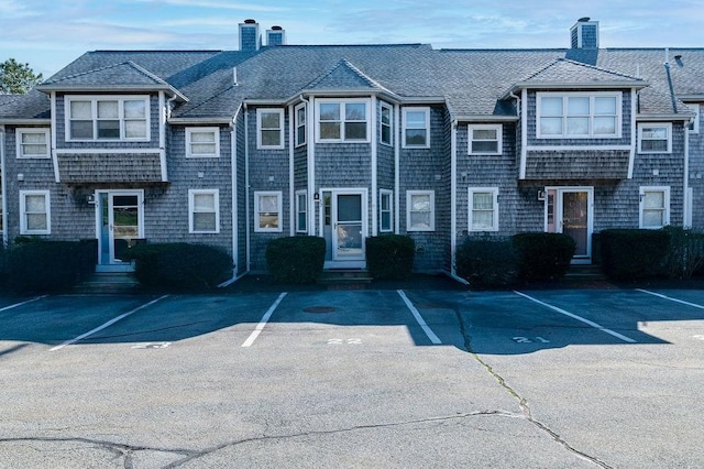 view of property with entry steps, uncovered parking, roof with shingles, and a chimney
