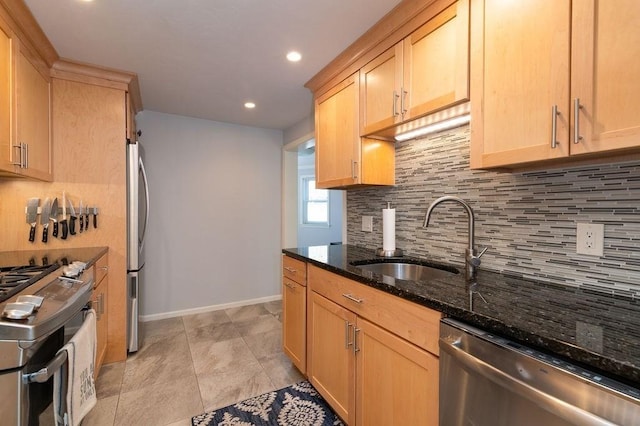 kitchen with backsplash, appliances with stainless steel finishes, a sink, baseboards, and dark stone countertops