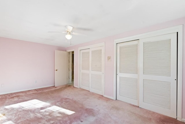 unfurnished bedroom with multiple closets, ceiling fan, and light colored carpet