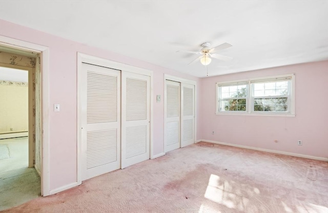 unfurnished bedroom with a baseboard radiator, multiple closets, ceiling fan, and light colored carpet