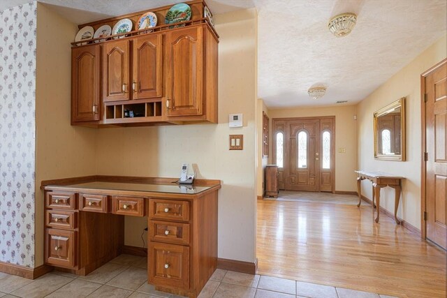 foyer entrance featuring light tile patterned floors, baseboards, a textured ceiling, and built in desk