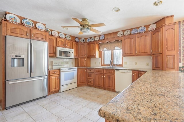 kitchen with a ceiling fan, a sink, tasteful backsplash, white appliances, and brown cabinetry
