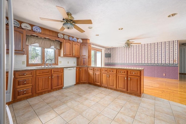 kitchen with wallpapered walls, a ceiling fan, white dishwasher, and a sink