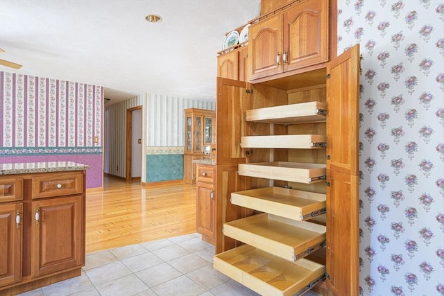 interior space with wallpapered walls, light stone countertops, light tile patterned floors, brown cabinets, and open shelves