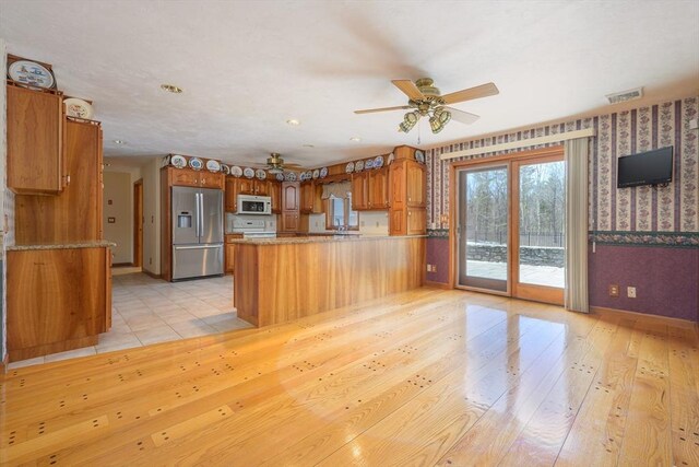 kitchen with stainless steel refrigerator with ice dispenser, a peninsula, brown cabinetry, wallpapered walls, and white microwave