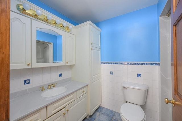 bathroom with wainscoting, vanity, toilet, and tile walls