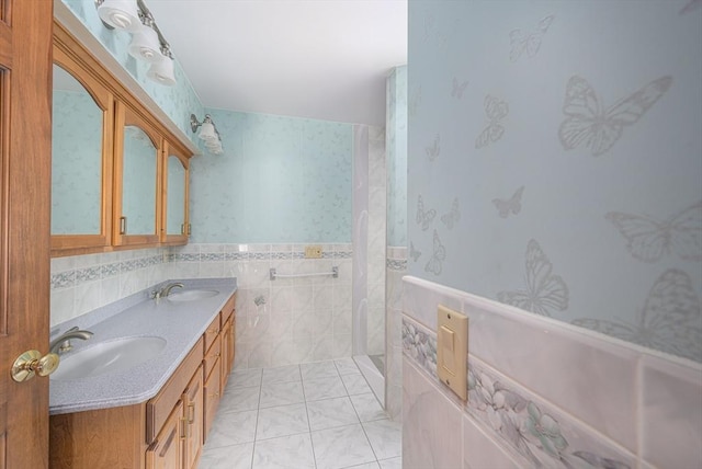 bathroom featuring tile patterned floors, a wainscoted wall, a sink, tile walls, and wallpapered walls