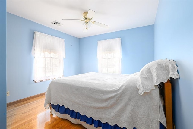 bedroom featuring baseboards, wood finished floors, visible vents, and ceiling fan