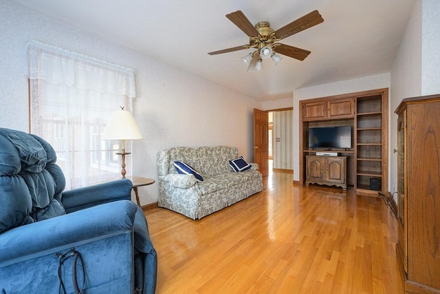 living room featuring baseboards, ceiling fan, and light wood finished floors