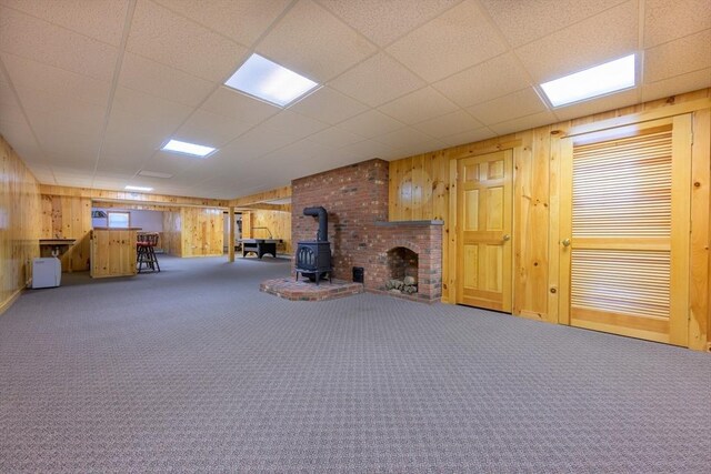 interior space featuring a wood stove, a drop ceiling, carpet, and wood walls