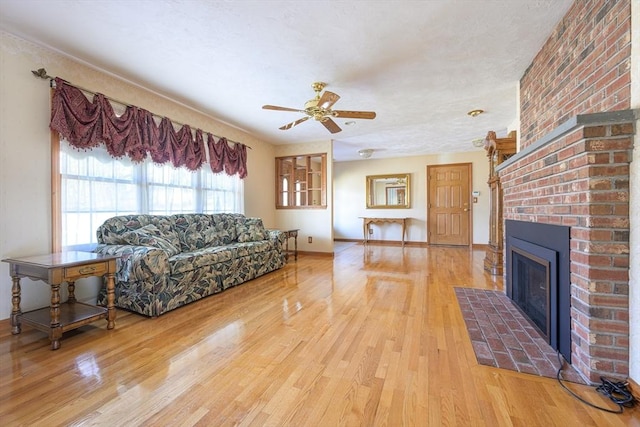 living area featuring a brick fireplace, baseboards, a ceiling fan, and wood finished floors