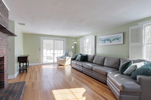 living room featuring light wood-type flooring, a brick fireplace, visible vents, and baseboards