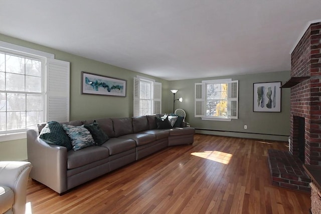 living room with a baseboard heating unit, a brick fireplace, wood-type flooring, and a healthy amount of sunlight