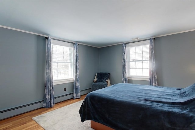 bedroom featuring ornamental molding, multiple windows, baseboard heating, and light wood-style flooring