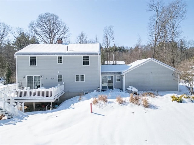 snow covered house with a garage, a chimney, and a wooden deck