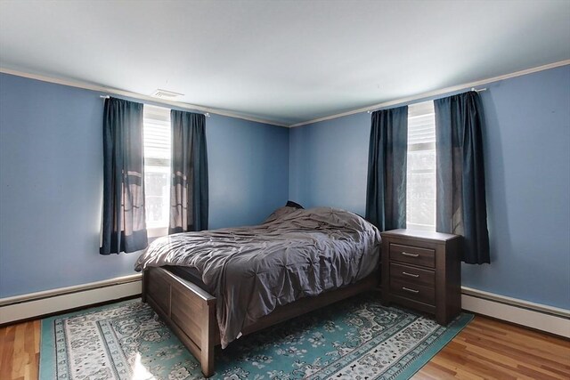 bedroom featuring a baseboard heating unit, crown molding, and light wood-style floors