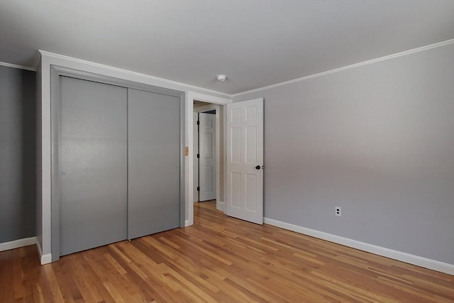 unfurnished bedroom with light wood finished floors, a closet, baseboards, and crown molding