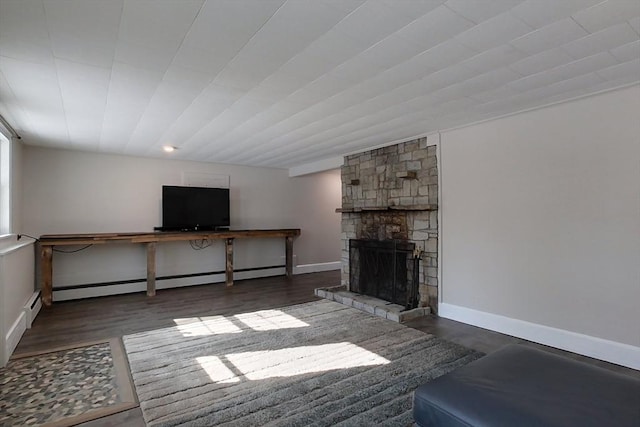 unfurnished living room featuring a stone fireplace, a baseboard radiator, dark wood finished floors, and baseboards