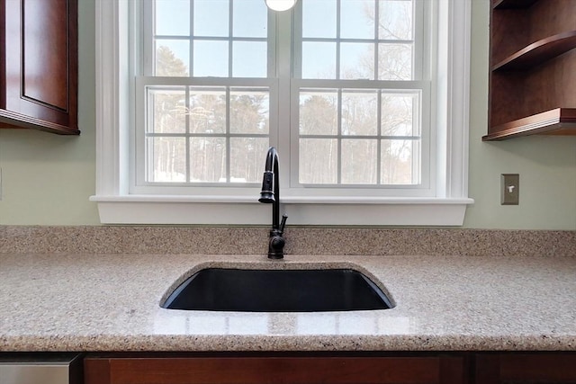 kitchen with open shelves, a sink, and light stone countertops