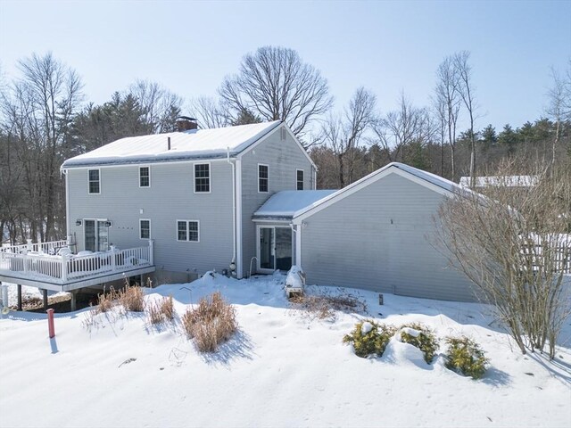 snow covered back of property with a garage, a chimney, and a wooden deck