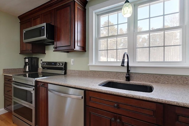 kitchen featuring stainless steel appliances, light countertops, a sink, and decorative light fixtures