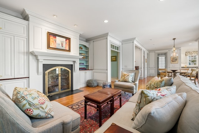 living room with ornamental molding, a large fireplace, hardwood / wood-style flooring, and built in shelves