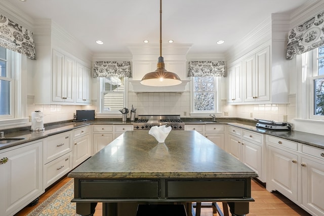 kitchen with hanging light fixtures, backsplash, a center island, white cabinets, and stove