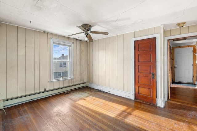 unfurnished room featuring hardwood / wood-style floors, wood walls, baseboard heating, and ceiling fan