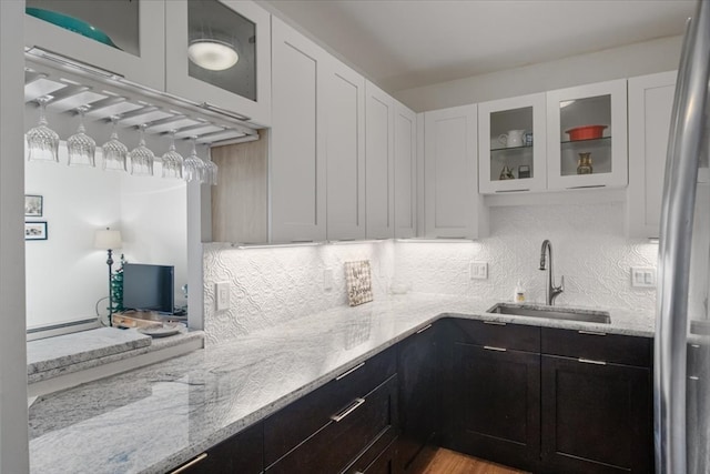 kitchen with light stone counters, white cabinetry, baseboard heating, and sink