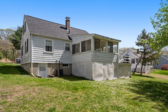 back of property featuring a chimney, a sunroom, cooling unit, a yard, and a shingled roof