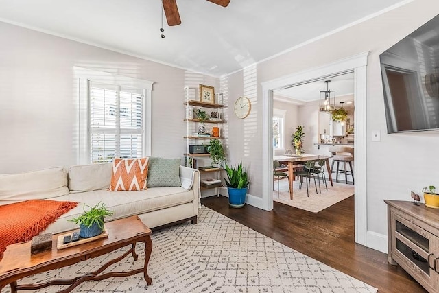 living room featuring dark wood-style floors, crown molding, baseboards, and ceiling fan