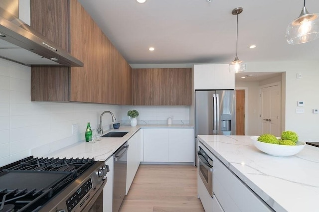 kitchen featuring sink, wall chimney exhaust hood, decorative light fixtures, white cabinetry, and stainless steel appliances