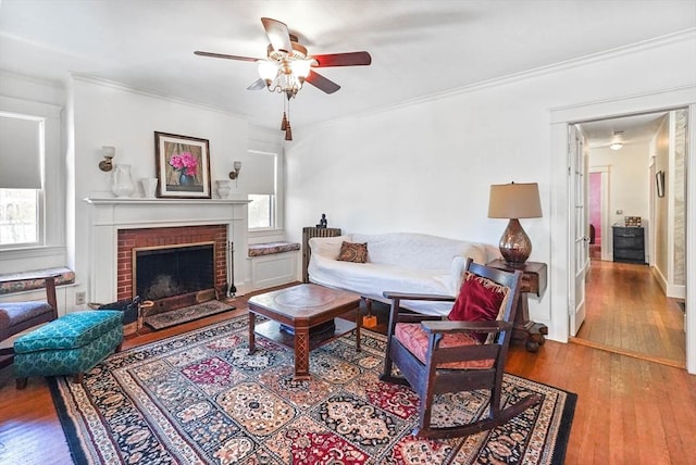 living room featuring hardwood / wood-style flooring, ornamental molding, a brick fireplace, and ceiling fan