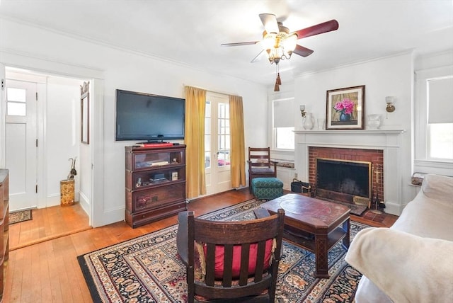 living room featuring a brick fireplace, wood-type flooring, ornamental molding, and ceiling fan