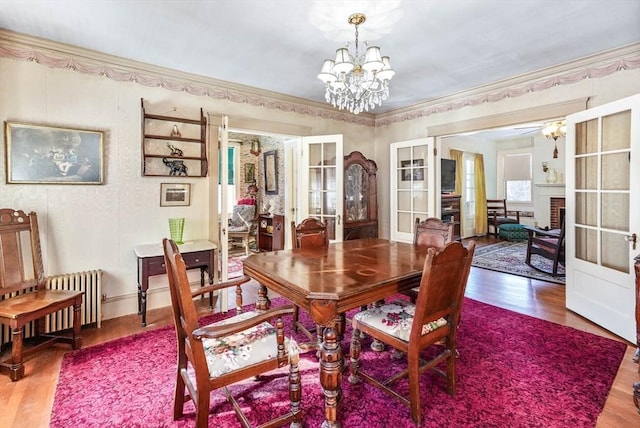 dining area with crown molding, hardwood / wood-style flooring, a notable chandelier, a brick fireplace, and french doors