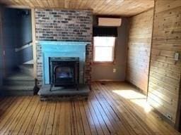 unfurnished living room with a wall unit AC, wooden ceiling, wood walls, a fireplace, and wood-type flooring