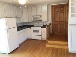 kitchen with dark countertops, white appliances, white cabinetry, and wood finished floors