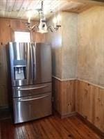 interior space featuring dark wood-style floors, a wainscoted wall, wooden walls, and stainless steel fridge with ice dispenser