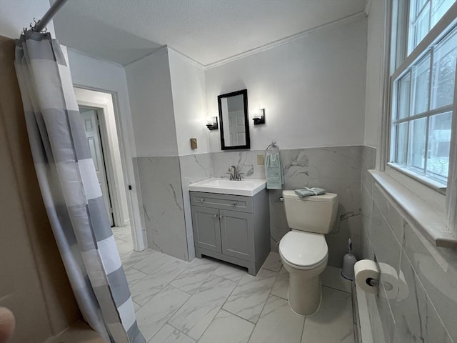 bathroom featuring a textured ceiling, toilet, vanity, marble finish floor, and wainscoting