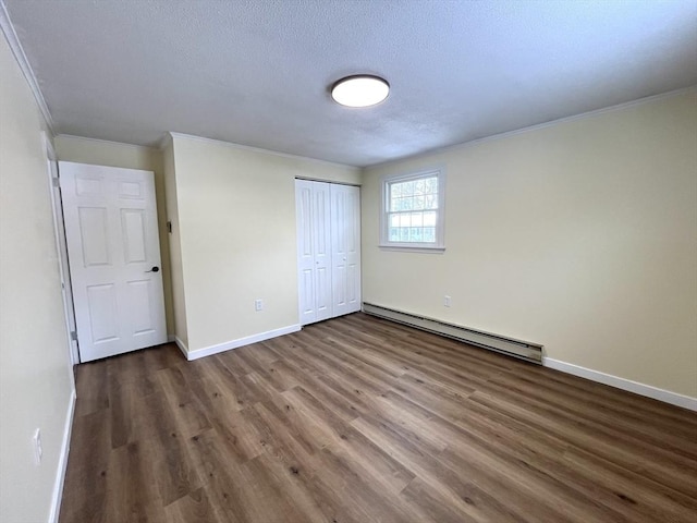 unfurnished bedroom with baseboards, ornamental molding, wood finished floors, baseboard heating, and a closet