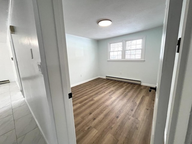 spare room with a baseboard heating unit, a textured ceiling, baseboards, and wood finished floors