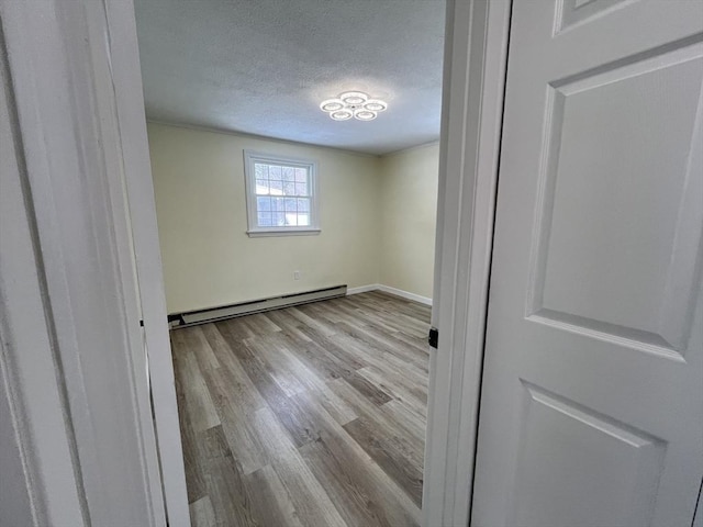 spare room featuring baseboards, baseboard heating, a textured ceiling, and wood finished floors