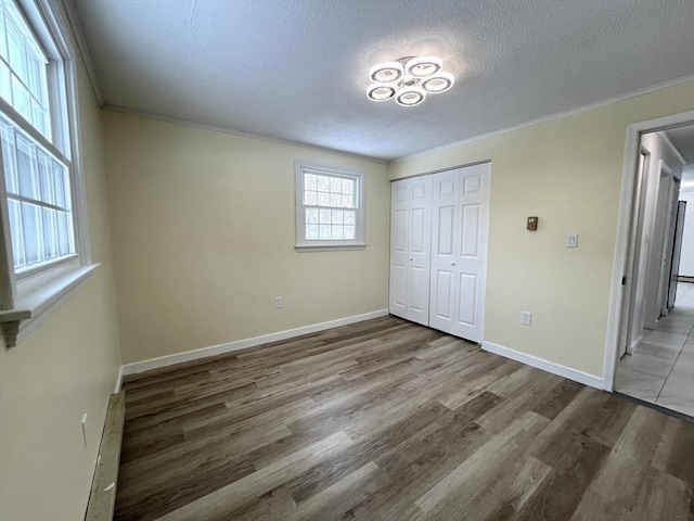 unfurnished bedroom featuring a textured ceiling, baseboards, wood finished floors, and crown molding